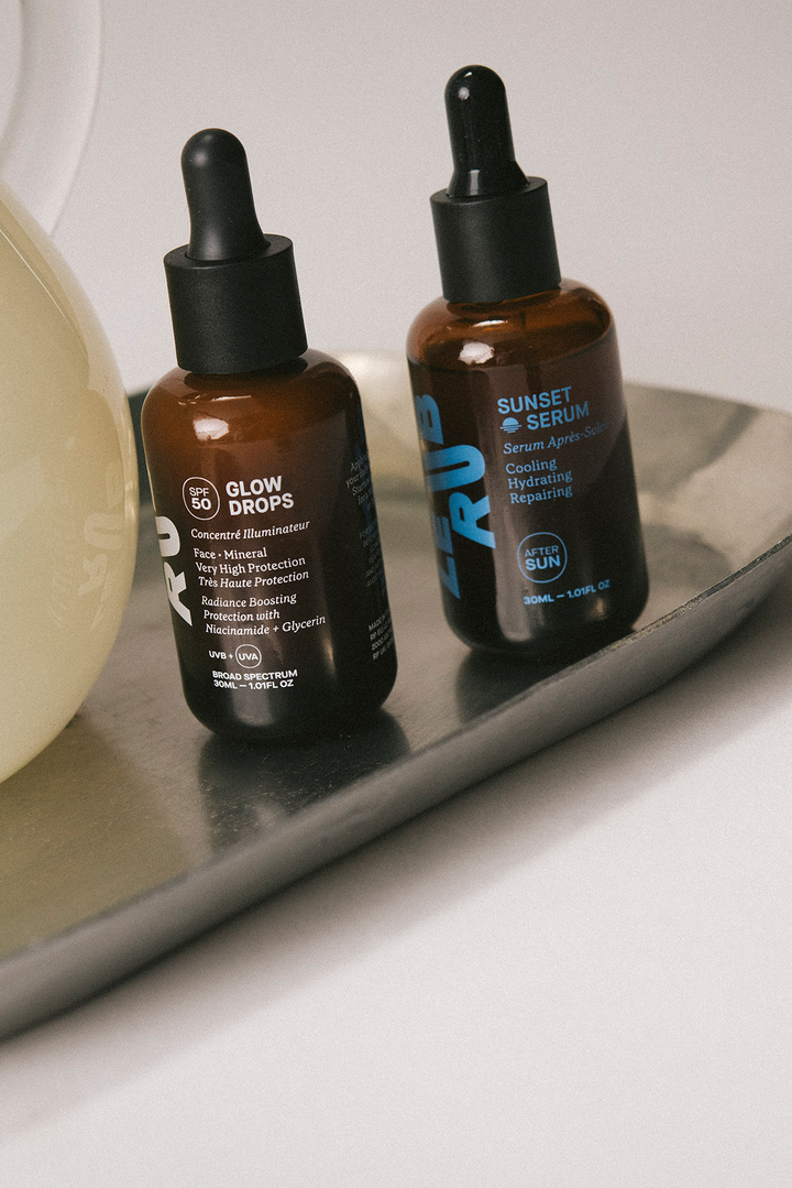 Two skincare serum bottles on a reflective surface with a neutral background