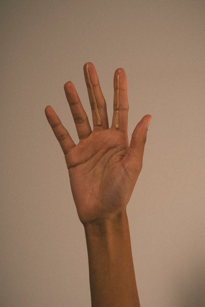 Hand raised against plain background showcasing texture and color of Glow Drops SPF50